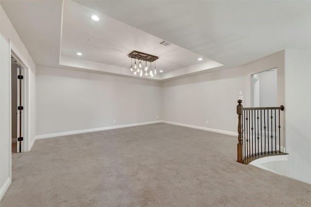 empty room featuring a tray ceiling, recessed lighting, light colored carpet, visible vents, and baseboards