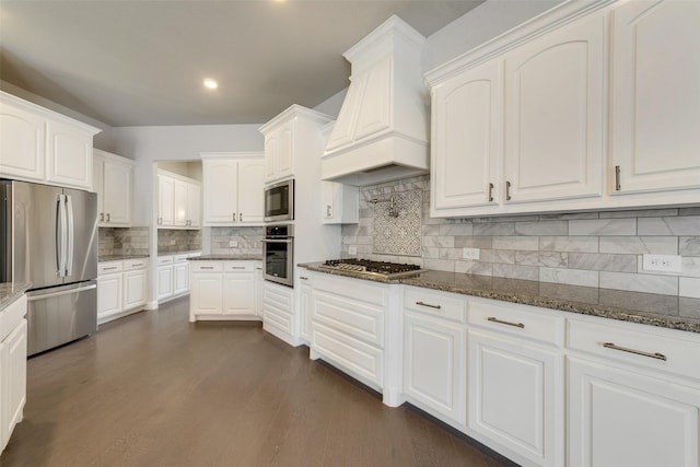 kitchen with dark wood-style floors, dark stone countertops, stainless steel appliances, premium range hood, and white cabinetry