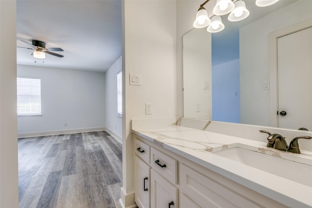 bathroom featuring ceiling fan with notable chandelier, vanity, baseboards, and wood finished floors