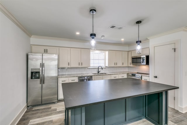 kitchen with visible vents, a kitchen island, appliances with stainless steel finishes, hanging light fixtures, and a sink