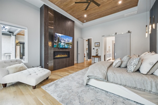 bedroom with a fireplace, a raised ceiling, light wood-style flooring, a barn door, and wood ceiling