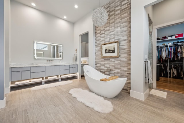 full bath featuring recessed lighting, a freestanding bath, a spacious closet, vanity, and wood finished floors