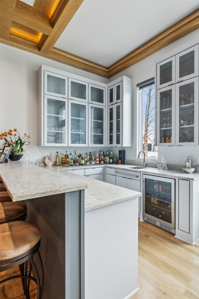 bar with beverage cooler, light wood finished floors, indoor wet bar, and a sink