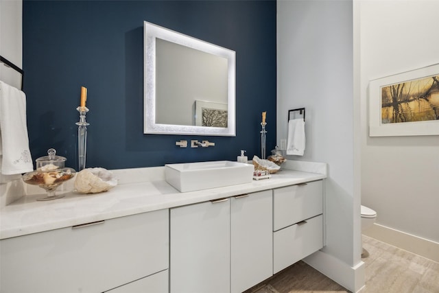 bathroom with baseboards, vanity, toilet, and wood finished floors