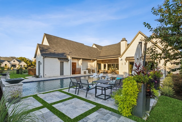 back of property featuring a shingled roof, an outdoor pool, a chimney, fence, and a patio area