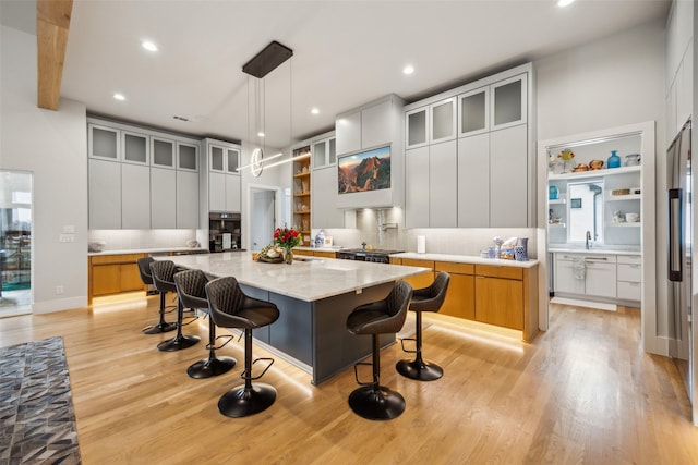 kitchen with light stone counters, a large island, hanging light fixtures, glass insert cabinets, and white cabinetry