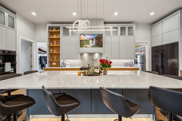 kitchen with high end fridge, a breakfast bar, modern cabinets, and glass insert cabinets