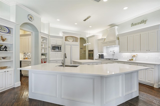 kitchen featuring built in appliances, light countertops, custom exhaust hood, open shelves, and a large island with sink