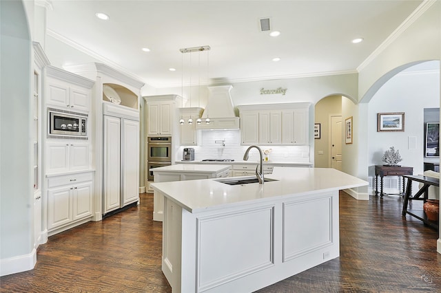 kitchen with decorative light fixtures, a center island with sink, light countertops, a sink, and premium range hood