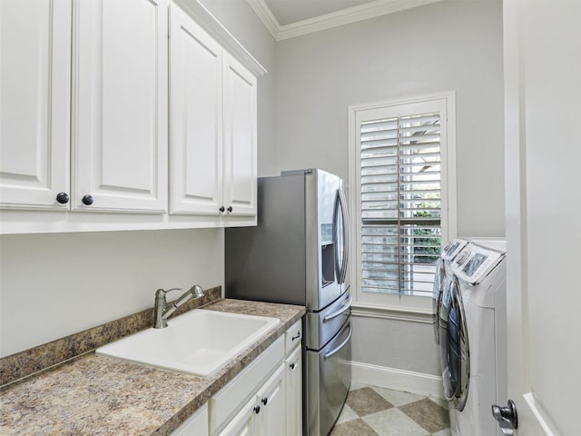 washroom featuring cabinet space, baseboards, crown molding, separate washer and dryer, and a sink