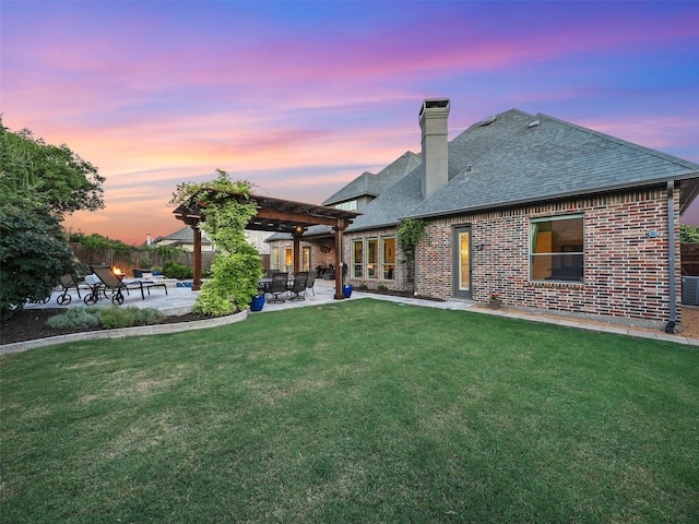 back of house at dusk with roof with shingles, fence, a yard, a patio area, and brick siding