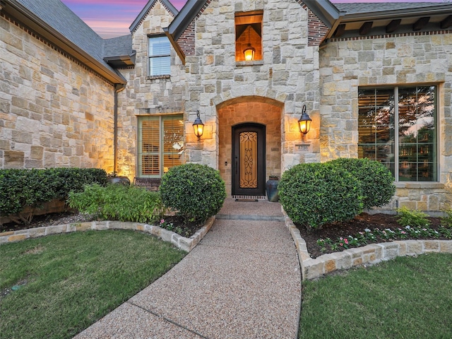 entrance to property featuring stone siding, a shingled roof, and a lawn