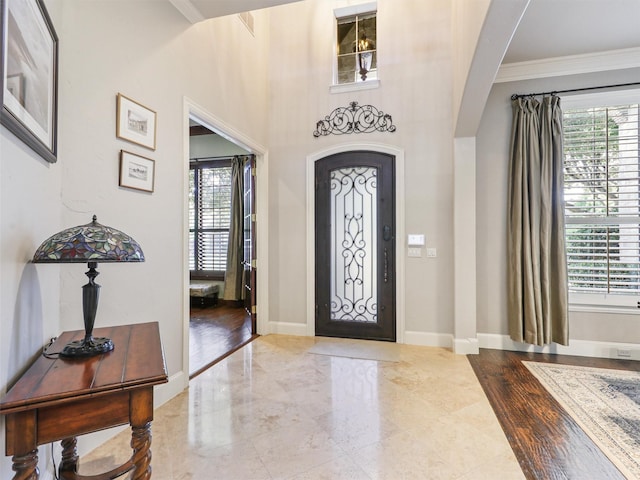 entrance foyer featuring arched walkways, baseboards, a wealth of natural light, and crown molding