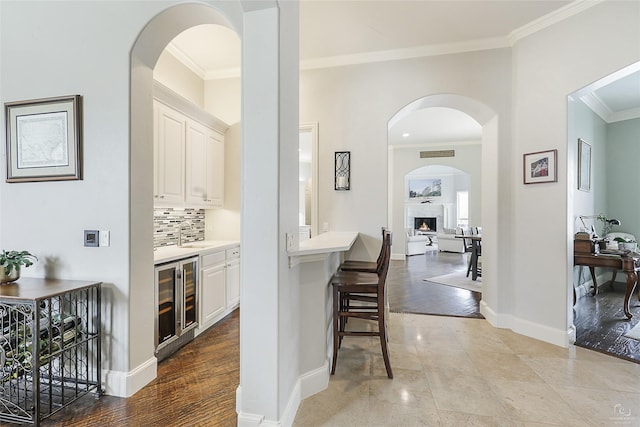 bar featuring wine cooler, crown molding, decorative backsplash, a lit fireplace, and baseboards