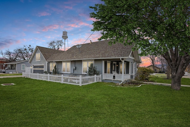 back of property at dusk featuring a garage, covered porch, a shingled roof, fence, and a lawn