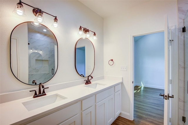 bathroom with double vanity, a sink, a marble finish shower, and wood finished floors