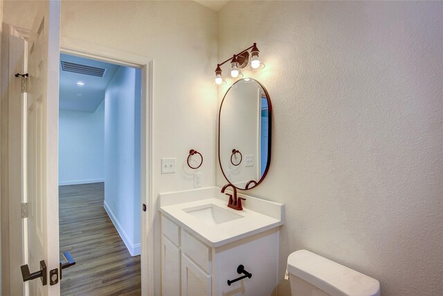 half bath with visible vents, toilet, vanity, wood finished floors, and baseboards