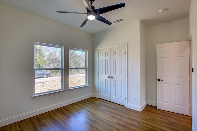 unfurnished bedroom with ceiling fan, visible vents, baseboards, a closet, and dark wood finished floors