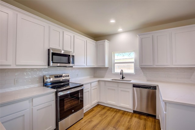 kitchen with light wood finished floors, stainless steel appliances, backsplash, white cabinetry, and a sink