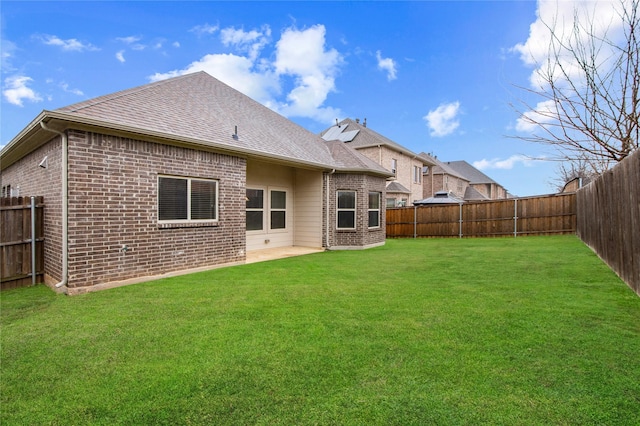 back of house with a fenced backyard, roof with shingles, a lawn, and brick siding