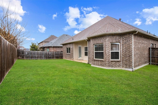 back of house featuring a yard, a fenced backyard, a shingled roof, and brick siding