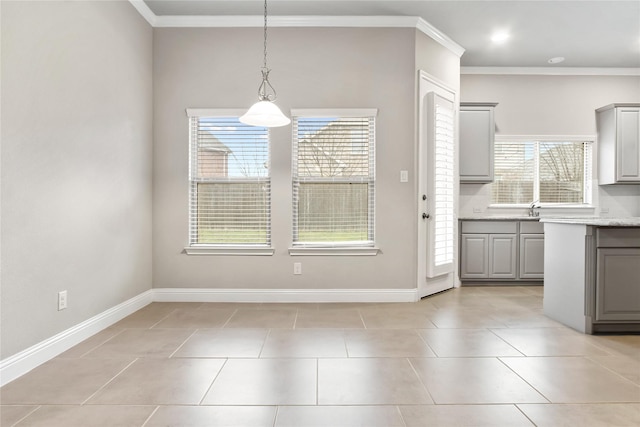 unfurnished dining area featuring light tile patterned floors, ornamental molding, a sink, and baseboards