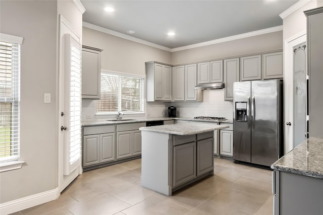 kitchen featuring light stone counters, under cabinet range hood, stainless steel appliances, a kitchen island, and a sink