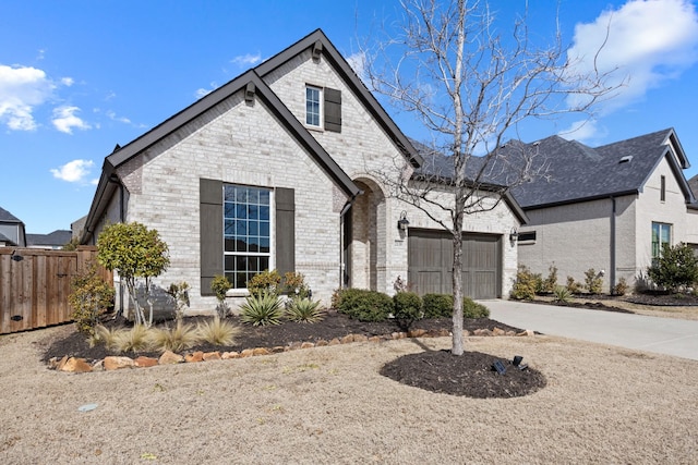 french provincial home featuring an attached garage, fence, concrete driveway, and brick siding