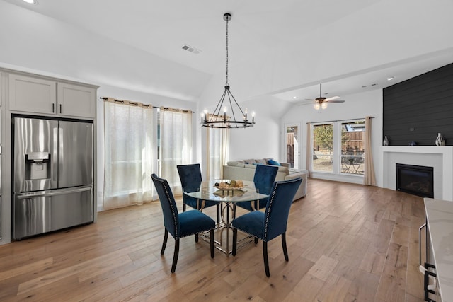 dining room with vaulted ceiling, light wood finished floors, a fireplace, and visible vents