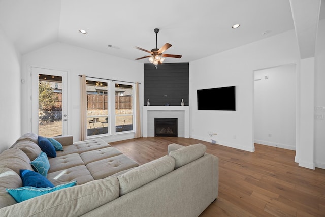 living area with a large fireplace, visible vents, vaulted ceiling, and wood finished floors