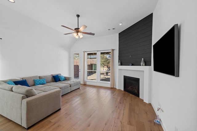 living room with a fireplace, lofted ceiling, visible vents, light wood-style floors, and ceiling fan