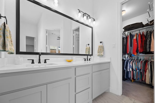 full bathroom with a walk in closet, marble finish floor, a sink, and double vanity