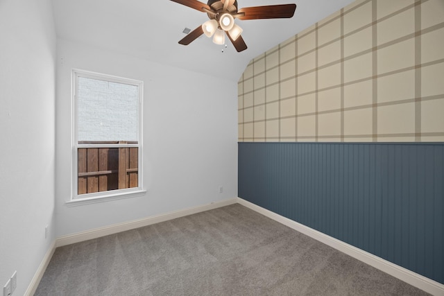 carpeted spare room featuring baseboards, vaulted ceiling, a ceiling fan, and wainscoting