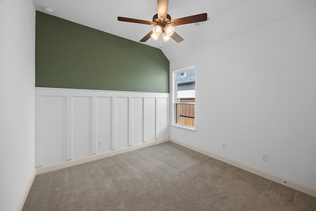 spare room with a wainscoted wall, vaulted ceiling, a ceiling fan, and light colored carpet