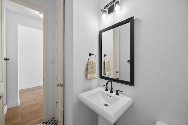 half bathroom featuring a sink, baseboards, and wood finished floors