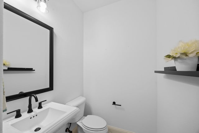 half bath with baseboards, a sink, and toilet