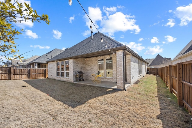 back of property featuring brick siding, a fenced backyard, a shingled roof, and a patio