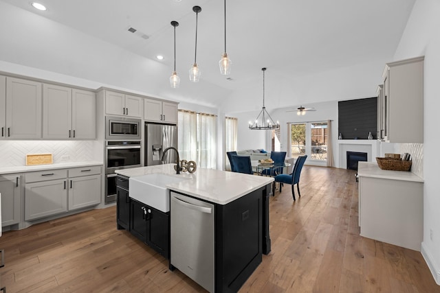 kitchen featuring appliances with stainless steel finishes, decorative light fixtures, a kitchen island with sink, gray cabinets, and light countertops