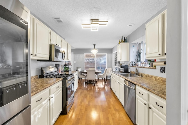 kitchen featuring light wood-style flooring, a sink, white cabinets, appliances with stainless steel finishes, and pendant lighting