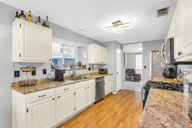 kitchen with light wood finished floors, visible vents, appliances with stainless steel finishes, white cabinetry, and a sink