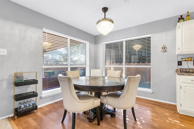 dining room with light wood-style floors, baseboards, a chandelier, and a textured ceiling