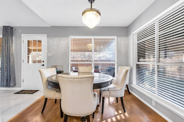 dining room featuring wood finished floors, a textured ceiling, baseboards, and an inviting chandelier