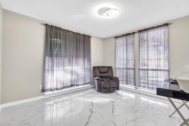 living area featuring a textured ceiling, marble finish floor, and baseboards