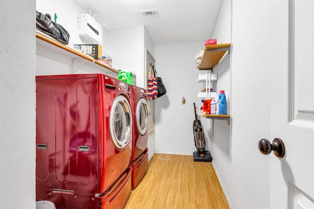 laundry room with laundry area, visible vents, wood finished floors, a textured ceiling, and washing machine and dryer