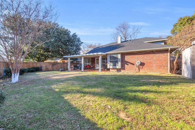 rear view of property featuring a chimney, brick siding, a lawn, and a fenced backyard