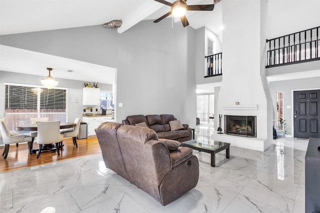 living area with vaulted ceiling with beams, marble finish floor, a large fireplace, and a ceiling fan