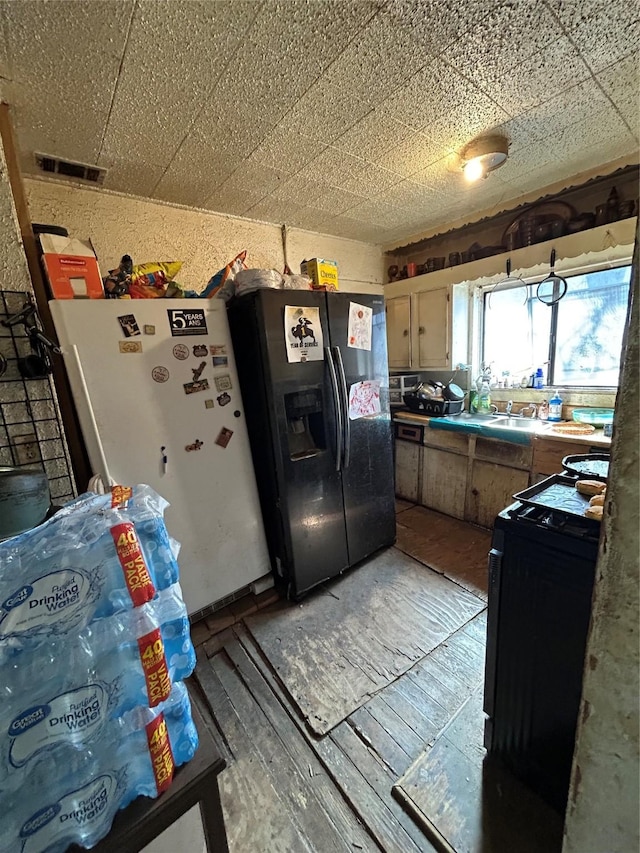 kitchen featuring wood finished floors, visible vents, black fridge with ice dispenser, range, and freestanding refrigerator