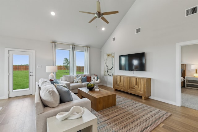 living area with high vaulted ceiling, light wood-style flooring, and visible vents