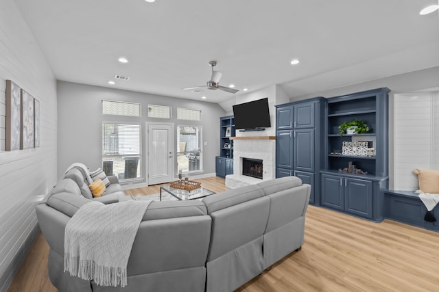 living area featuring light wood-style flooring, a fireplace with raised hearth, and recessed lighting