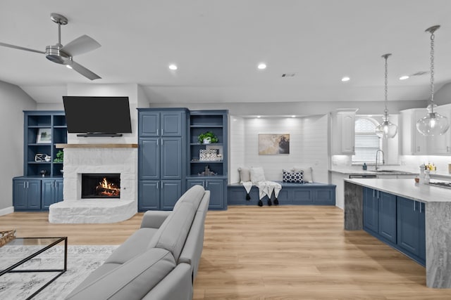 living room featuring light wood-style flooring, ceiling fan, a stone fireplace, and recessed lighting